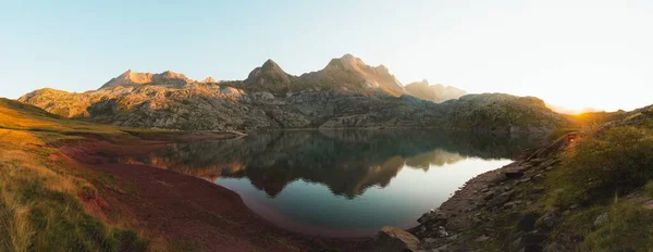 Dağların panoramik görüntüsü bir göle yansıyor, bir kız sol tarafta yürüyor.