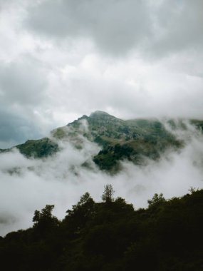 Bulutlu bir günde bulutların arkasına bakan dağ.