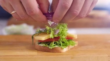 Aşçı hamburgerin üzerine ince soğan dilimleri koyar. Mutfakta kahvaltı için nefis sandviçler pişiriyorum. Fast food. Çıtır tostlu hamburger ve haşlanmış yumurta. Domatesli ve peynirli bir sandviç.