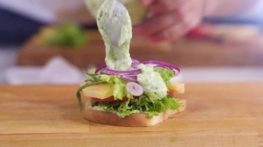 Hamburgerin üzerine bir kaşık baharatlı sos serpiştirdim. Büyük lezzetli sandviçli kahvaltı hazırlıyorum. Sağlıklı beslenme kavramı. Fast food. Çıtır tostlu hamburger ve haşlanmış yumurta. Domates peynirli sandviç yapıyorum.