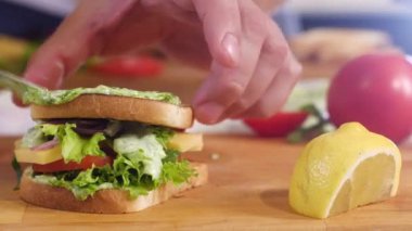 Kabuklu ekmek tostlu sandviç ve haşlanmış yumurta. Evin mutfağındaki aşçı bir hamburger topluyor. Bir adam ekmeğin üzerine pesto sosu, olgun domates dilimleri, soğan dilimleri ve peynir parçaları koyar..