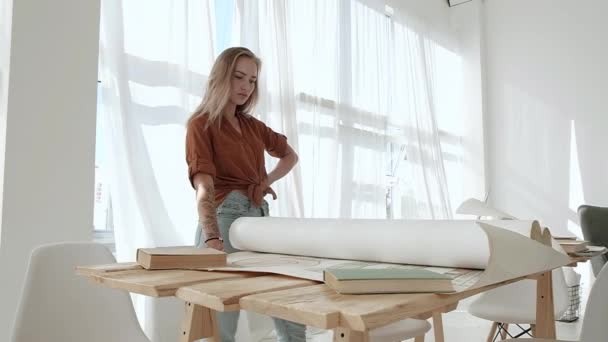 사무실에 커다란 윈도우가 귀여운 소녀는 프로젝트 두루마리와 그리고 펼치는 그림들을 — 비디오