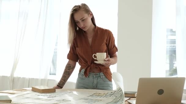 방에서 프로젝트를 건축가 디자이너입니다 여자는 그림과 설계도를 활기넘치는 커피를 마신다 — 비디오