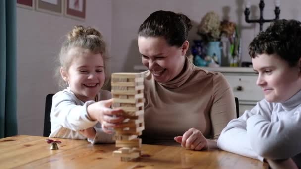 快乐的年轻妈妈和两个可爱的孩子玩耍 一位爱开玩笑的母亲帮助学龄前儿童在客厅里建造一座木制的塔楼 与整个家庭的教育游戏 — 图库视频影像
