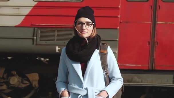 年轻独立迷人的女孩背负着背包站在火车站站台上面对过往的客运列车的肖像 乘火车独立旅行的概念 — 图库视频影像
