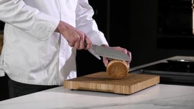 Beyaz önlüklü profesyonel şef restoran mutfağında keskin bıçakla hamburger ekmeği kesiyor. Sokak yemeği. Lezzetli hamburgerler pişiriyorum. Yemek için malzemelerin hazırlanması.