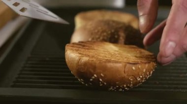 Profesyonel erkek aşçı kızarır ve kızgın ızgarada dilimlenmiş çöreğe dönüşür. Lokanta mutfağında lezzetli hamburgerler pişirmek. Malzemelerin hazırlanması. Lezzetli ev yapımı hamburgerlerle barbekü.