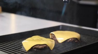 Mutfakta aşçı lezzetli hamburger için et köfteleri ve dilimlenmiş taze peynirle hazırlar. Şef, kıtır kıtır yemek için gaz tüpünden sulu et kızartması yapıyor. Sokak yemekleri hamburger yapıyor. Sandviç yapıyorum