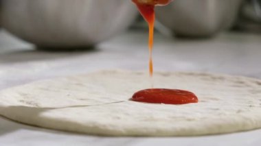 Baker geleneksel İtalyan pizzası hazırlar. Mutfaktaki restoranda pizza pişirmek. Şef pizza hamuruna kepçeyle domates sosu sürer. Pizzacıda pizza yapma süreci