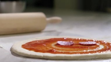 Profesyonel fırıncı geleneksel ev yapımı İtalyan pizzası hazırlıyor. Mutfaktaki restoranda pizza pişirmek. Aşçı çiğ hamura ince dilimler halinde pepperoni sosisi koyar. Pizzacıda pizza yapma süreci.
