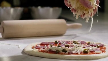 Profesyonel fırıncı geleneksel İtalyan pizzasını hazırlar. Mutfaktaki bir restoranda pizza pişirmek. Aşçı çiğ hamurun üzerine rendelenmiş peynir döker. Pizzacıda pizza yapma süreci..