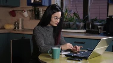 Akşamları genç ve çekici Asyalı bir kadın mutfakta oturup dizüstü bilgisayarla çalışıyor. Kız bilgisayara bir mesaj yazar ve kahve içer.