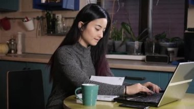 Genç ve çekici Asyalı kadın serbest yazar evde, mutfakta dizüstü bilgisayar üzerinde çalışıyor. Kız bilgi aramak için internette geziniyor ve bilgisayara bir mesaj yazıyor.