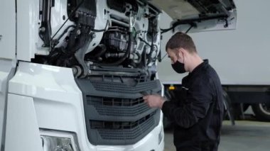 Tamir servisindeki profesyonel müfettiş. Üniformalı ve koruyucu maskeli bir erkek tamirci, arızaları aramak ve kargo taşımacılığını teşhis etmek için modern bir cihaz tableti kullanıyor.