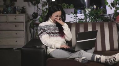 Mutlu Asyalı kadın sıcak kazağı akşamları apartmanın kanepesinde oturuyor ve bir dizüstü bilgisayar üzerinde çalışıyor. Serbest çalışan bir kız evdeki bilgisayarda arkadaşlarıyla görüntülü konuşma yoluyla mesaj yazar.