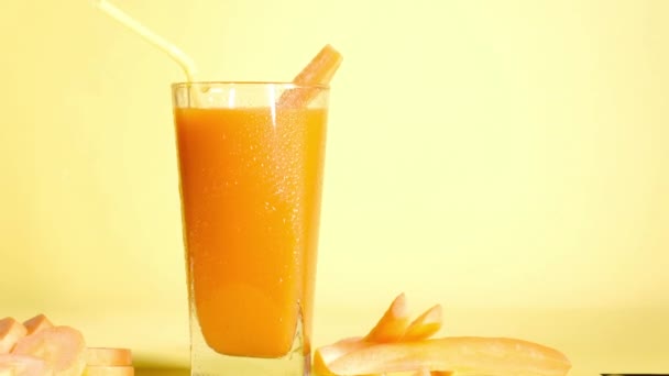 健康滑滑的有机胡萝卜汁蔬菜片和在黄色背景下的玻璃杯中的鸡尾酒管 新鲜蔬菜 健康食品和饮料 天然配料中的维生素混合物 — 图库视频影像