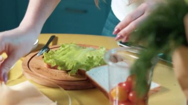 Ev mutfağında çekici genç bir bayan lezzetli bir sandviç hazırlıyor tost, peynir, salata ve jambonlu. Kız tostun üzerine bir parça marul, peynir ve jambon koyar. Her sabah taze kahvaltı.