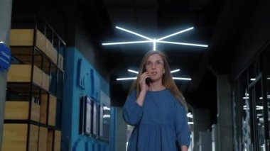 Başarılı bir iş kadını ofis içi akıllı telefonla konuşur. İş kadını koridorda yürüyor ve cep telefonuyla konuşuyor. İş merkezinin koridorunda yürüyen dost canlısı bir kadının portresi..