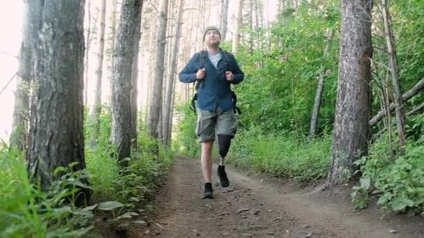 バックパック付き義肢を持つ障害者は 森の中を歩くと道を克服し 楽しむ 森林道路に沿って徒歩で旅行し 障害者のためのアクティブなライフスタイル 活動的なハイキング — ストック動画