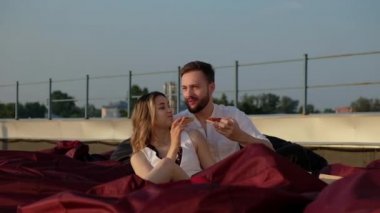 Genç beyaz adam ve kız yaz akşamının günbatımında yumuşak koltuklarda binanın çatısında oturuyorlar. İnsanlar pizza yer ve eğlenir. Birbirine aşık çiftlerin çatısında buluşacağız. Erkek arkadaş sevgiliye sarılır.