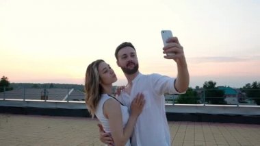 Yakışıklı bir adam ve çekici bir Avrupalı kız gün batımında çatıda dinleniyorlar. Aşık bir çift modern bir akıllı telefondan selfie çeker ve mutlu bir şekilde güler. Romantik geleneksel ilişkiler