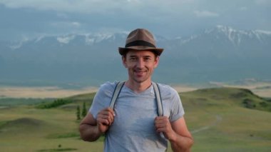 Dağ vadisinde yürüyüş yapan erkek turistin portresi, yaz manzarası. Yürüyüşçü kameraya bakar ve mutlulukla gülümser..