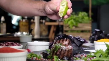 Mutfaktaki ızgara biftekler baharat ve otlarla dolu bir tahtaya konur. Pişmiş etin üzerine taze limon suyu döker. Et pişirmek. Mutfakta barbekü.