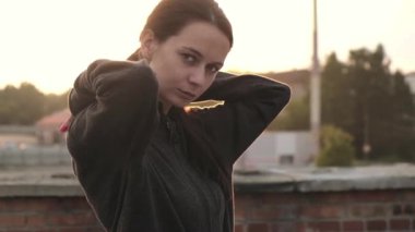 Gün batımına karşı çatıda duran güzel, beyaz, güçlü ve kendine güvenen bir kadının portresi. Sporcu kadın boksör egzersizden önce kapüşon takar. Kendine güvenen bir kadının kardiyo eğitimi dışında