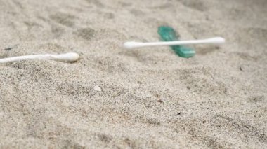 Düşen deniz çöpleri yavaş çekimde, pamuklu çubuklar, jilet ve sigaralar kirli sahilde atılıyor, okyanus kirliliği