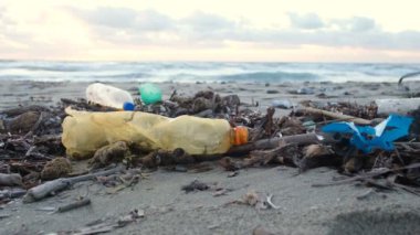 İnsan, kirlenmiş okyanus kıyılarından, gün batımından, çevresel atıklardan, plastik şişeleri topluyor.