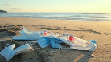Yüz maskeleri ve el dezenfektanı atıkları günbatımında deniz kıyısı ekosistemine atılıyor.