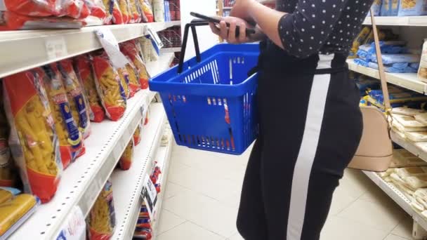 Κορίτσι κάνουν ψώνια σε ένα σούπερ μάρκετ με busket ψώνια και smartphone, ζυμαρικά τροφίμων — Αρχείο Βίντεο