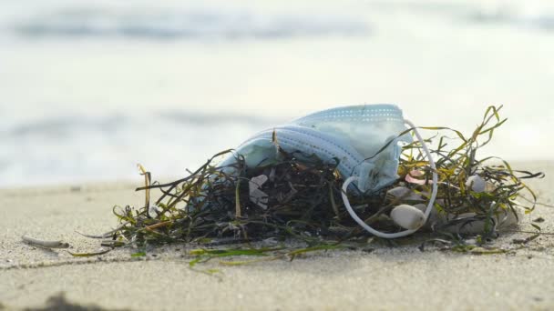 海の生態系に捨てられた保護面マスクを使用し、人々はバックグラウンドで歩く、医療用のカバー19汚染 — ストック動画