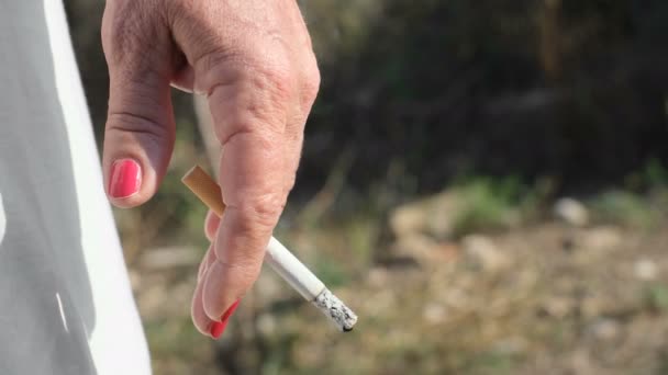 Пожилая женщина держит горящую сигарету во время курения, табачный дым, нездоровый образ жизни — стоковое видео