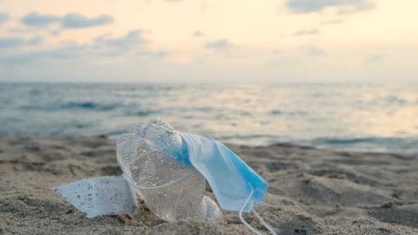 Захисна маска для обличчя та пластикова пляшка, викинута на морську екосистему, відходи забруднення московитів — стокове відео
