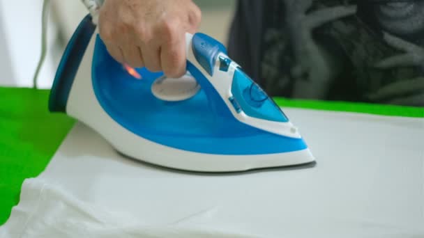 Elderly woman hand while ironing clothes with a steam iron on an Ironing board — Stock Video