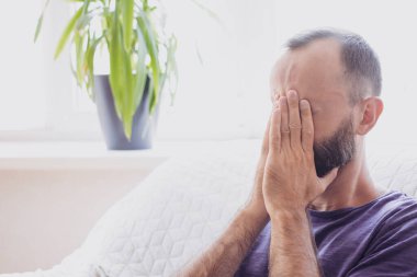 Üzgün depresif esmer adam elleriyle yüzünü kapatıyor, ağlıyor, evdeki kanepede oturuyor. Umutsuzluk, psikolojik sorun, keder, alkol ve uyuşturucu sorunları yaşıyor. Boşluğu kopyala.