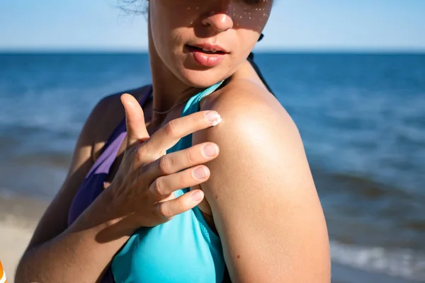 Applying sunscreen protection lotion spf. Young woman putting suntan solar cream to her shoulder to protect skin from burns, premature aging and skin cancer, dressed blue swimsuit.Ocean in background