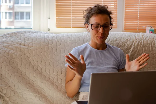 Genç esmer kadın dizüstü bilgisayardaki video konferans başvurusunu kullanarak konuşuyor, evdeki kanepede oturuyor. Özel ders, müşteriyle çevrimiçi görüşme, webinar, internet kullanarak eğitim sınıfı dersi.