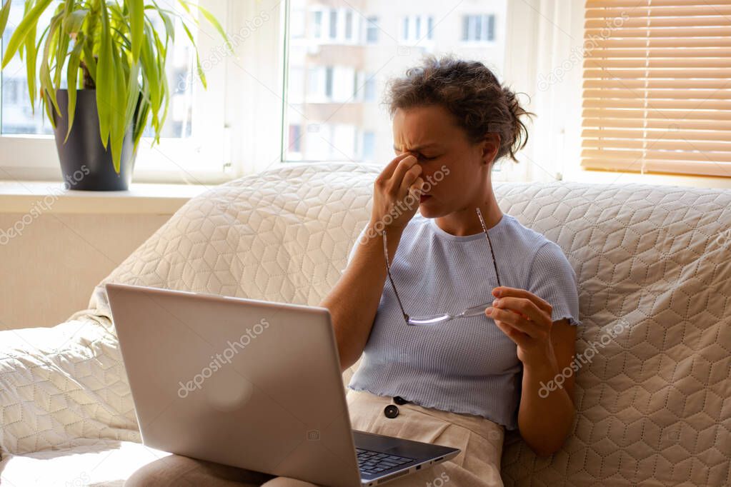 Tired young woman after computer work, keeping eyes closed and massaging nose, taking off glasses. Overworked female freelancer suffering from blurry vision after long laptop use, eye strain problem