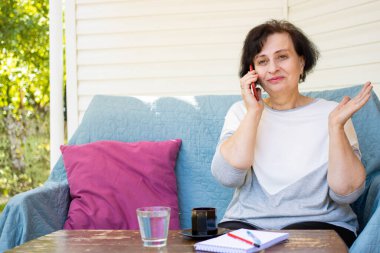 Mutlu, heyecanlı, son sınıf öğrencisi bir kadın iyi habere şaşırmış, cep telefonuyla konuşuyor, şaşırmış hissediyor, açık terasta kanepede oturuyor. Hoş sohbetler. Beklenmedik bir galibiyet, satış teklifi.