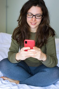 Elinde akıllı telefon olan güzel bir kız öğrenci. Kapalı bir odada oturuyor ve 5G kablosuz internet bağlantısı kullanıyor. Sosyal medyayı, video görüşmesini, web sitesini, sohbeti, online alışverişi kontrol ediyorum. Dikey