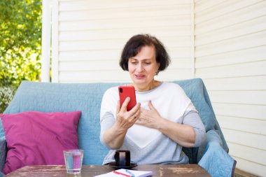 Duygusal olarak mutlu, son sınıf öğrencisi bir kadın online video görüşmesi yapıyor, akıllı telefona bakıyor, iletişim uygulamasını kullanarak yurtdışında oturan çocuklarla konuşuyor.