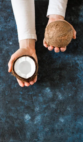 Eine weibliche Hand reicht eine ganze Kokosnuss und eine halbe Kokosnuss — Stockfoto
