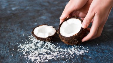 Kadın elleri hindistan cevizinin iki yarısını dokulu mavi mermer arka planda tutuyor.