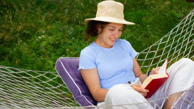 Güzel esmer kız ilginç bir kitap okuyor. Bahçede hamakta oturuyor, yaz tatilinin keyfini çıkarıyor. Saman şapka takıyor, sınavı geçmeye hazırlanıyor.