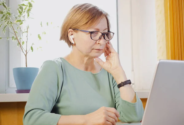 Ev ofisinde dizüstü bilgisayarla çalışmakla meşgul yaşlı bir iş kadını. Bilgisayarda yazma, interneti arama, web sitesini tarama. Olgun öğrenci çevrimiçi çalışıyor, ses kurslarını dinliyor, Webinar