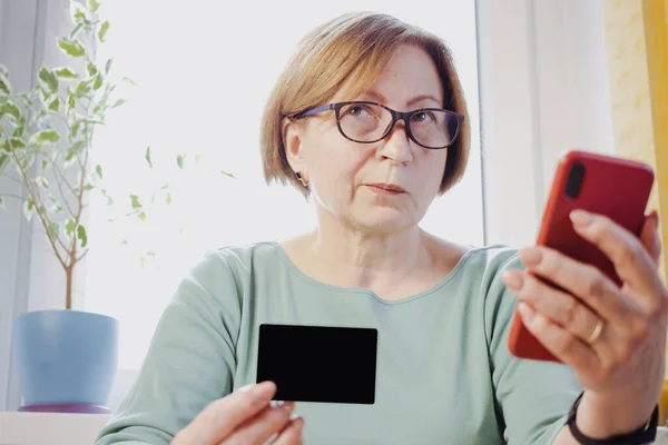 신용 카드를 들고 집에 앉아 있는 스마트폰을 이용해 혼란 스러워 하는 유럽의 상류층 여성 이 실망했습니다. 빚 문제, 실패한 거래, 돈 문제 . 노인 세대와 기술 — 스톡 사진