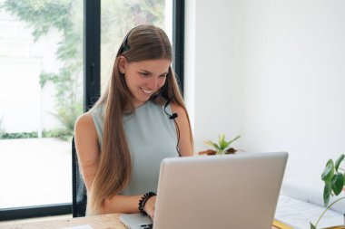 Bilgisayarı kullanarak kulaklık takan, gülümseyen bir öğrenci.