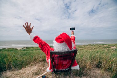 Öforik Noel Baba 'nın arka görüntüsü. Tatilde, akıllı telefonuyla selfie çekiyor. Modern Noel zamanı.